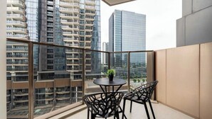 A balcony with a table and chairs, a potted plant, and a view of high-rise buildings. - The Opera D2 Apartment  (Ho Chi Minh City)