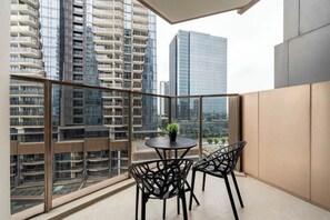 A balcony with a table and chairs, a potted plant, and a view of high-rise buildings.