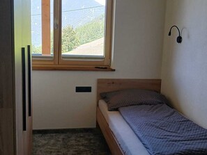A small, single-bed room with a window, a bedside table, and a wall-mounted light fixture. - Panoramic View Apartment Kaunergrat (Kaunerberg)