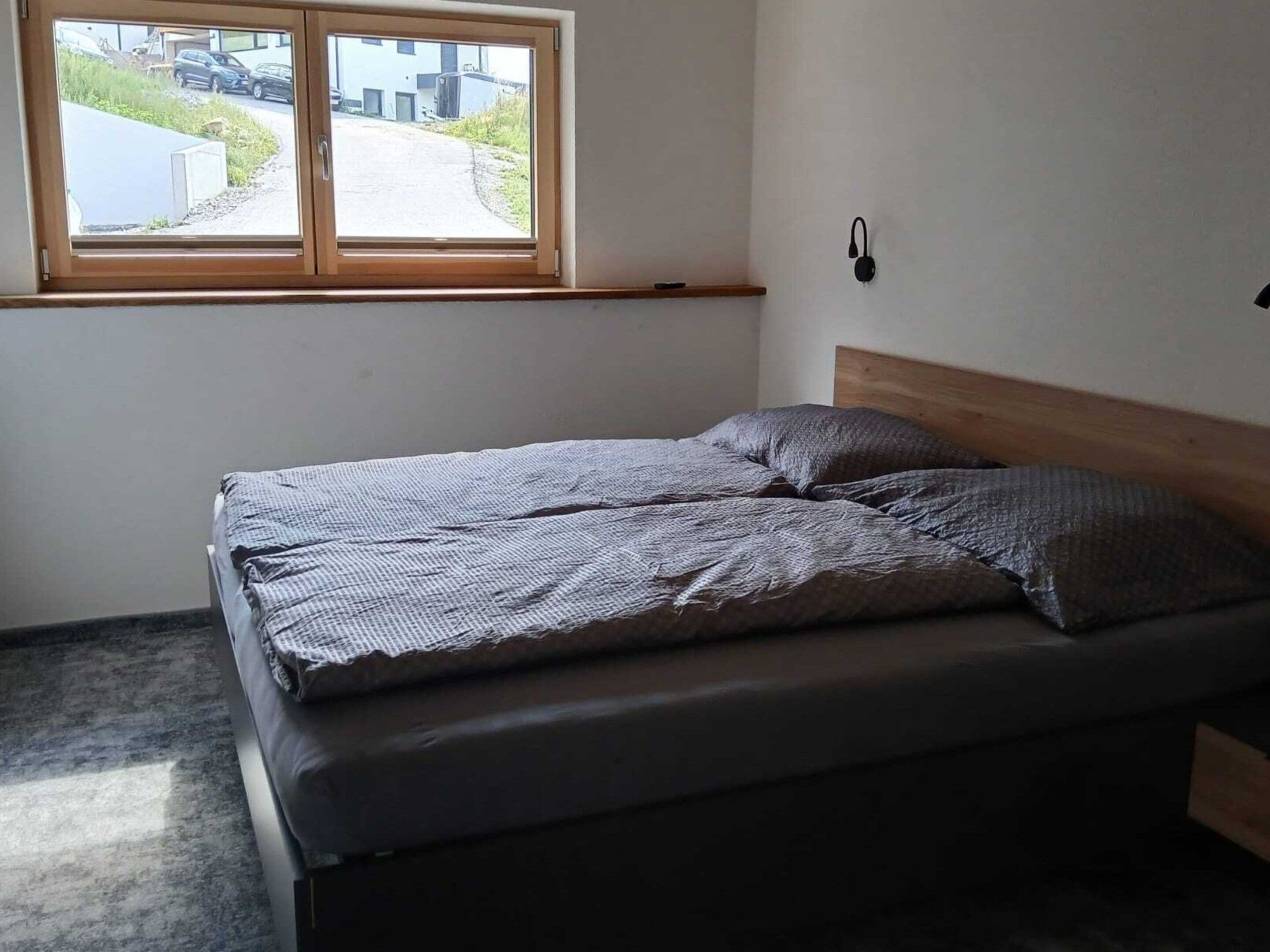 A single bed with a wooden headboard in a room with a window.