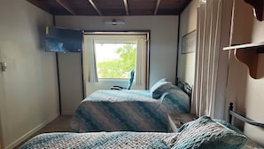 Quarto com duas camas, uma televisão presa na parede e uma janela com cortinas.