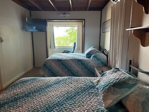 Ein Zimmer mit zwei Betten, einem an der Wand befestigten Fernseher und einem mit Vorhängen versehenen Fenster.