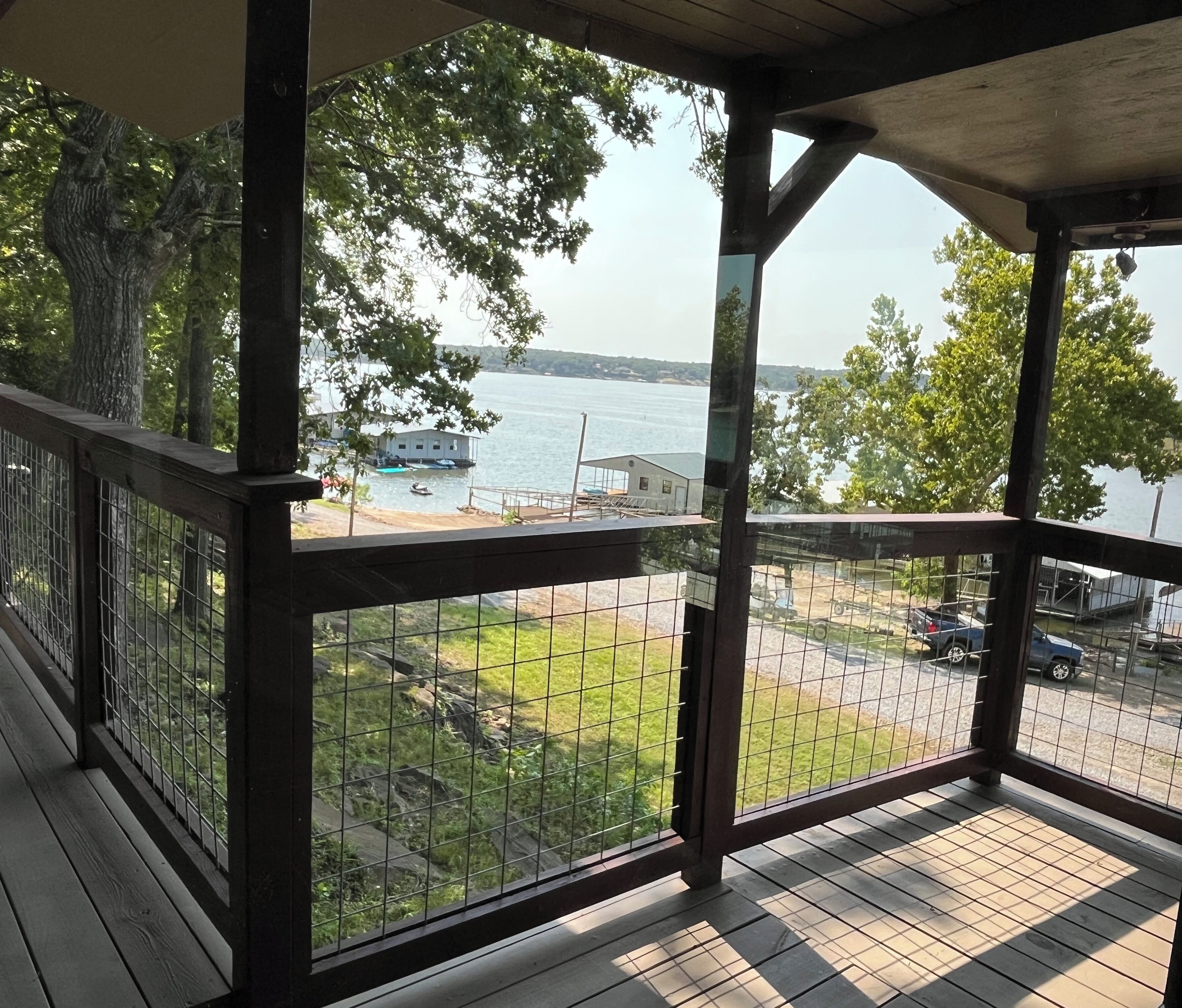 A covered outdoor area with a view of a body of water, a dock, and a grassy area with a fence.