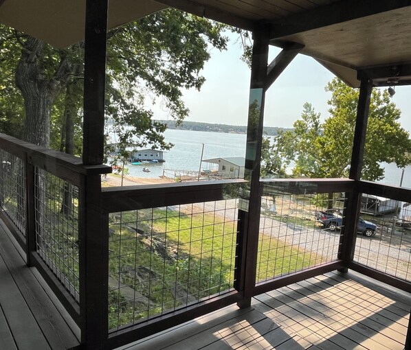A covered outdoor area with a view of a body of water, a dock, and a grassy area with a fence.