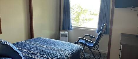 Una habitación con una cama, una silla, un escritorio y una ventana con cortinas.