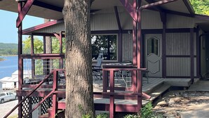 Uma cabana com varanda, área de estar coberta e vista para o lago.