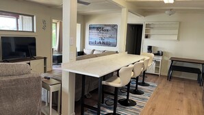 Uma cozinha moderna com bancada de mármore, banquetas de bar e uma área de refeições com uma mesa grande.