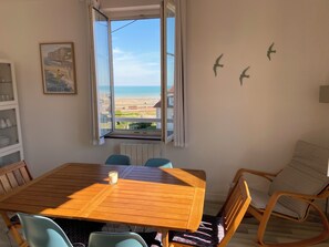 Ein Essbereich mit Tisch und Stühlen, ein Fenster mit Blick auf den Strand und eine Wand mit Vogelkonturen.