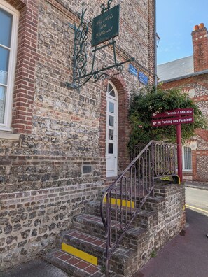 Ein historisches Gebäude mit einer Steinfassade, einem Schild mit der Aufschrift 'Les Arts du Piloteau' und Hinweisschildern für 'Tennis/Mairie' und 'Parking des Failles'.