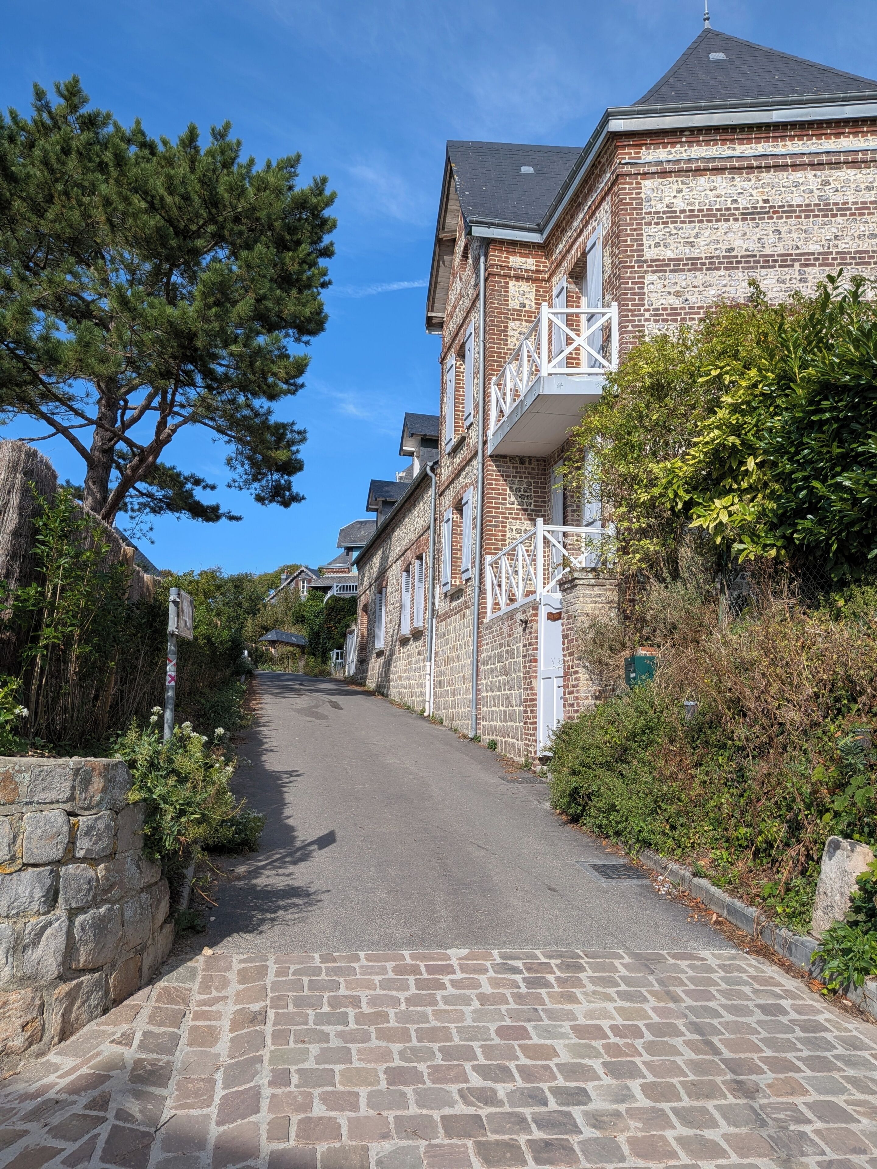 Eine schmale Straße, gesäumt von traditionellen Backsteingebäuden mit Balkonen, einer Steinmauer auf einer Seite und einem Baum auf der anderen.
