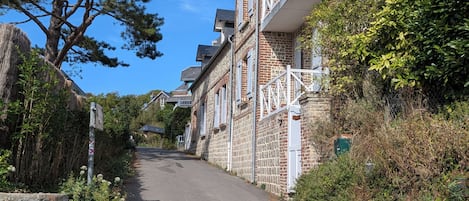Eine schmale Straße, gesäumt von traditionellen Backsteingebäuden mit Balkonen, einer Steinmauer auf einer Seite und einem Baum auf der anderen.