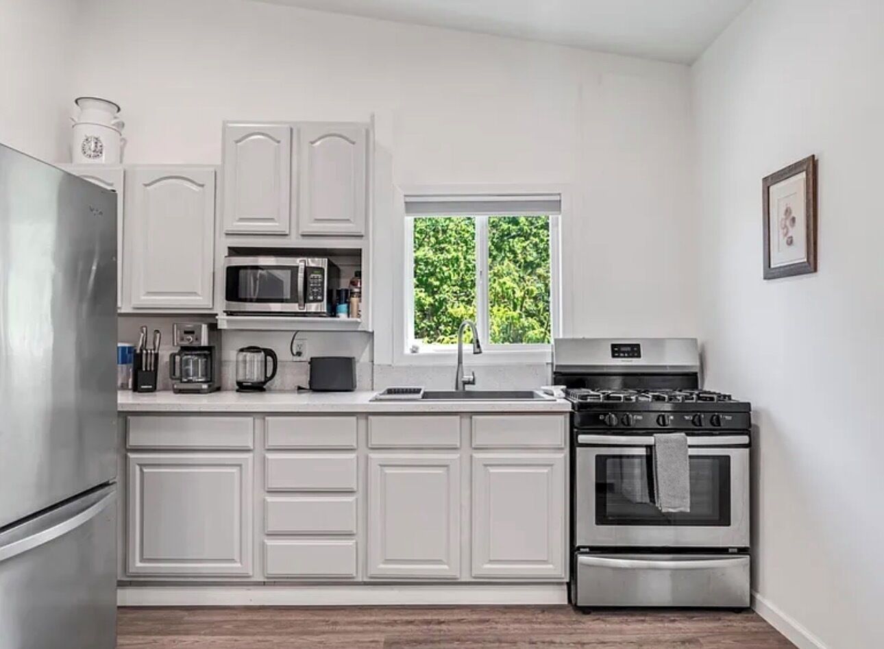 A modern kitchen with white cabinetry, stainless steel appliances, and a window providing a view of greenery outside.