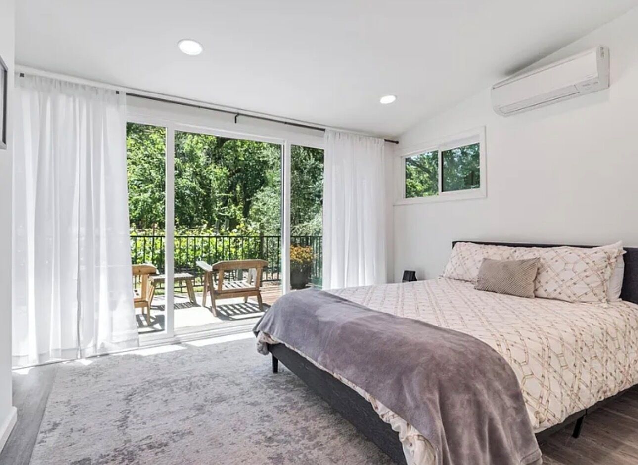 A bedroom with a bed, a sliding glass door to a balcony, and a ceiling-mounted air conditioning unit.