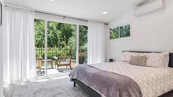 A bedroom with a bed, a sliding glass door to a balcony, and a ceiling-mounted air conditioning unit.