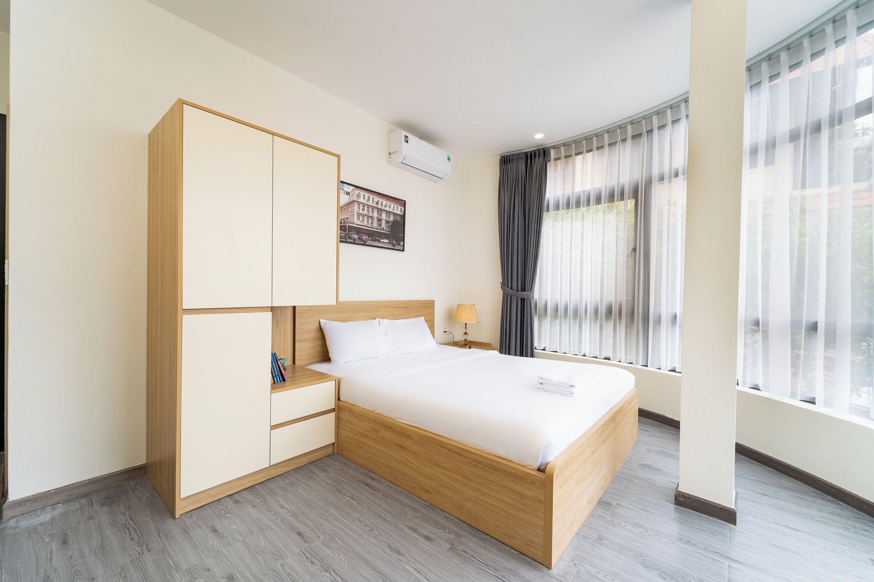 Habitación de hotel con cama, armario, mesita de noche, lámpara y ventana con cortinas.