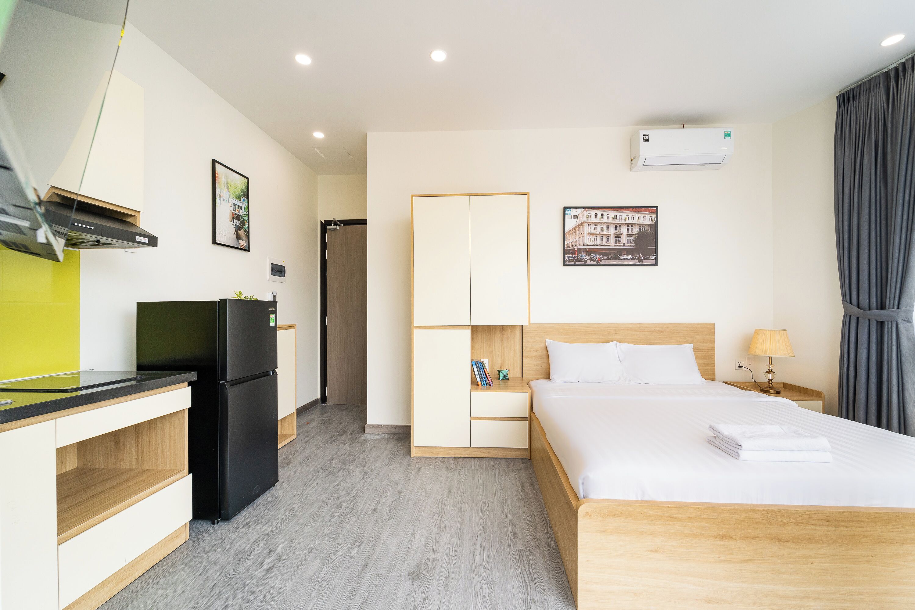 A hotel room with a bed, bedside table, lamp, and a refrigerator.