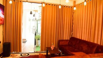 A living room with a sofa, a small table, and curtains. There is a speaker and a plant visible.