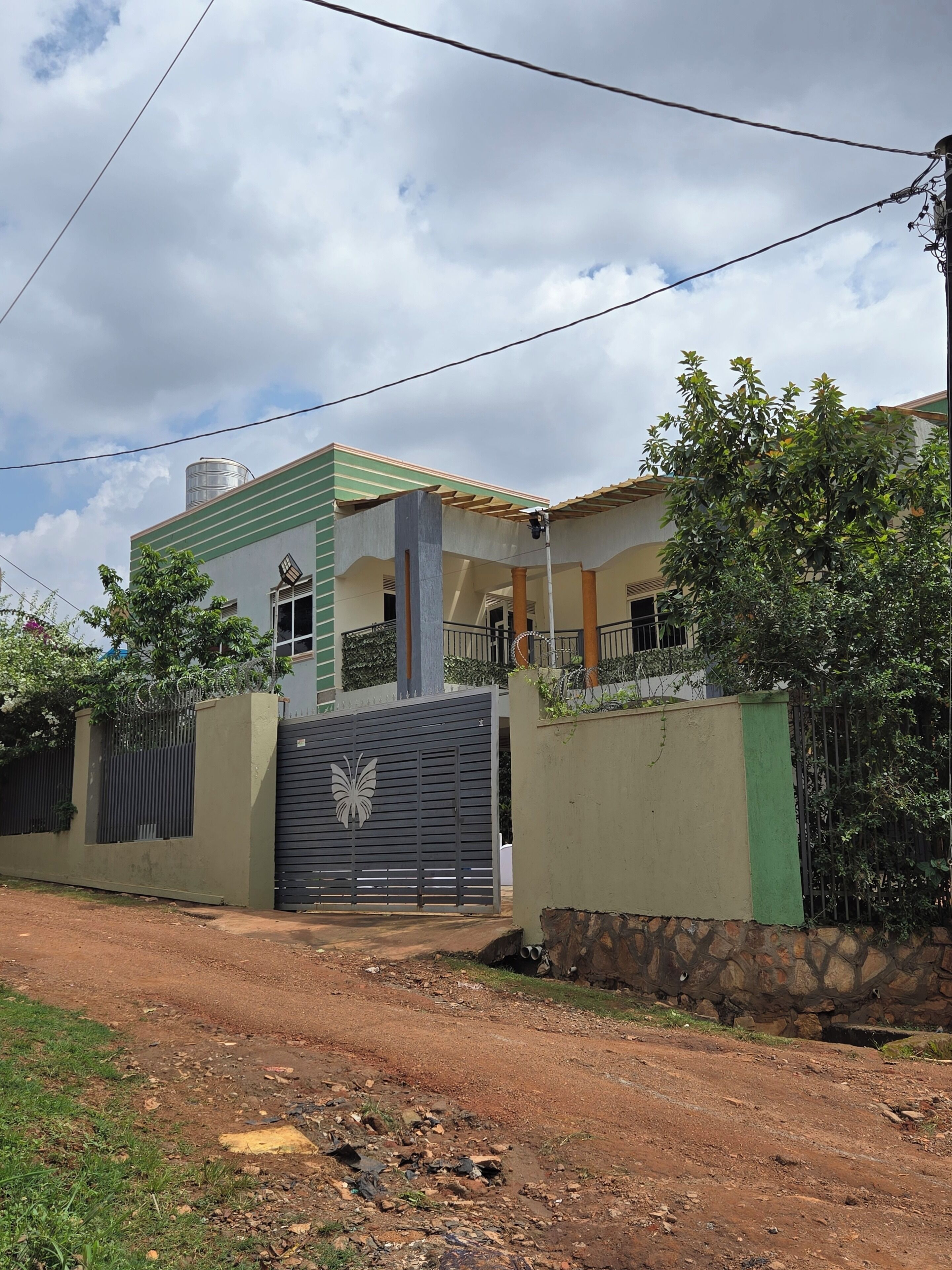 A residential property with a gated entrance, a water tank on the roof, and a paved driveway.