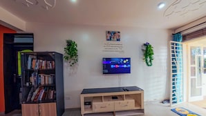 Ein Wohnzimmer mit Flachbildfernseher an der Wand, einem Bücherregal, einer Holz-Unterhaltungsanlage und einer Tür, die nach draußen führt.