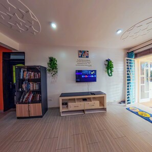 Ein Wohnzimmer mit Flachbildfernseher an der Wand, einem Bücherregal, einer Holz-Unterhaltungsanlage und einer Tür, die nach draußen führt.