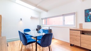 Un comedor moderno con una mesa de vidrio y sillas azules, un armario de madera y una ventana con persianas.