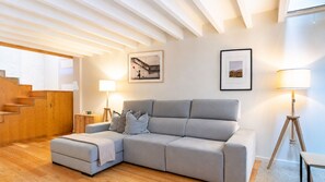 Una sala moderna con un sofá seccional gris, piso de madera, una escalera y dos lámparas fijadas a la pared.