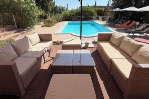 Un área junto a la piscina con mobiliario de mimbre, una piscina y una zona de estar techada.