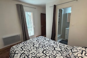 A bedroom with a bed, a window with curtains, a door leading to a bathroom, and a radiator.