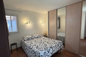 Ein Schlafzimmer mit Bett, Nachttisch, Lampe, Fenster und Kleiderschrank.
