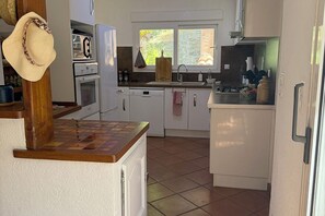 Ett kök med vita skåp, en träbänkskiva och ett fönster med utsikt över grönområden.