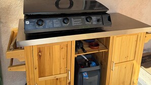 Ein schwarzer, tragbarer Grill auf einem Holzschrank mit einem Metallregal darunter.