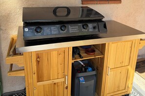 En svart, bärbar grill placerad på ett träskåp med en hylla i metall under.