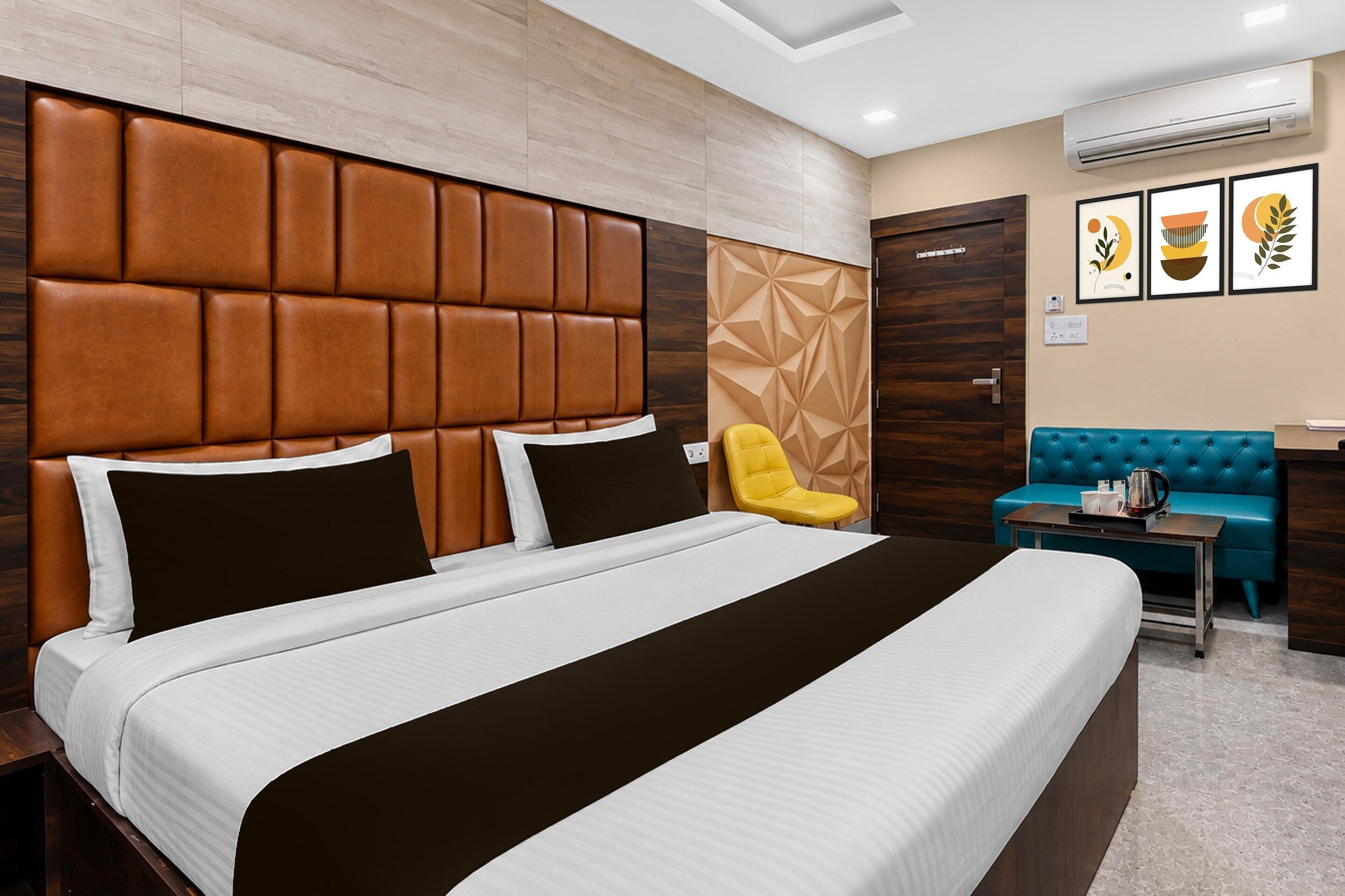 A hotel room with a large bed, a sofa, a chair, and a small table with a kettle.