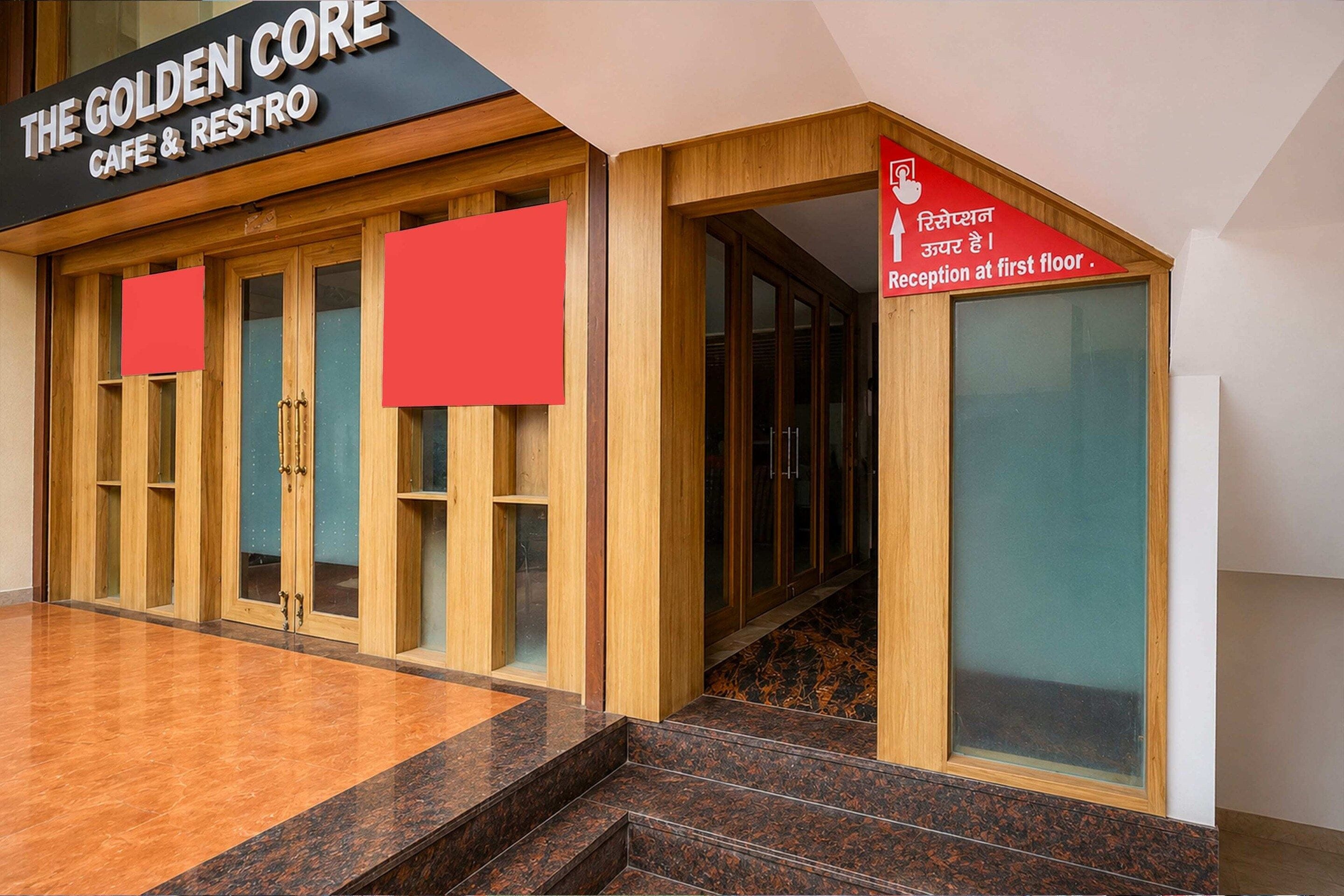 Une entrée d’immeuble avec une enseigne indiquant « The Golden Core Cafe & Restro » et un panneau de signalisation indiquant la direction à suivre pour accéder à la réception, située au premier étage.