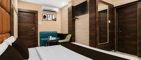A hotel room with a bed, a seating area with a table, a TV mounted on the wall, and a wardrobe.