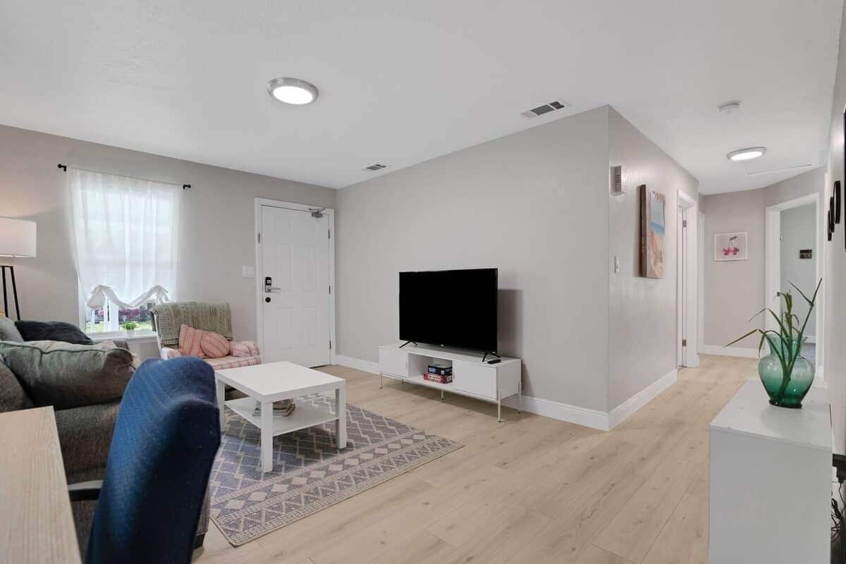 A modern living room with a flat-screen TV, a white coffee table, a sofa, and a patterned rug.
