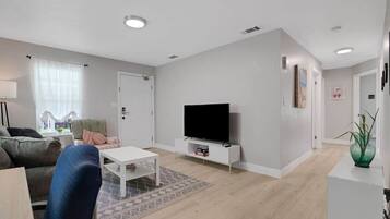 A modern living room with a flat-screen TV, a white coffee table, a sofa, and a patterned rug.