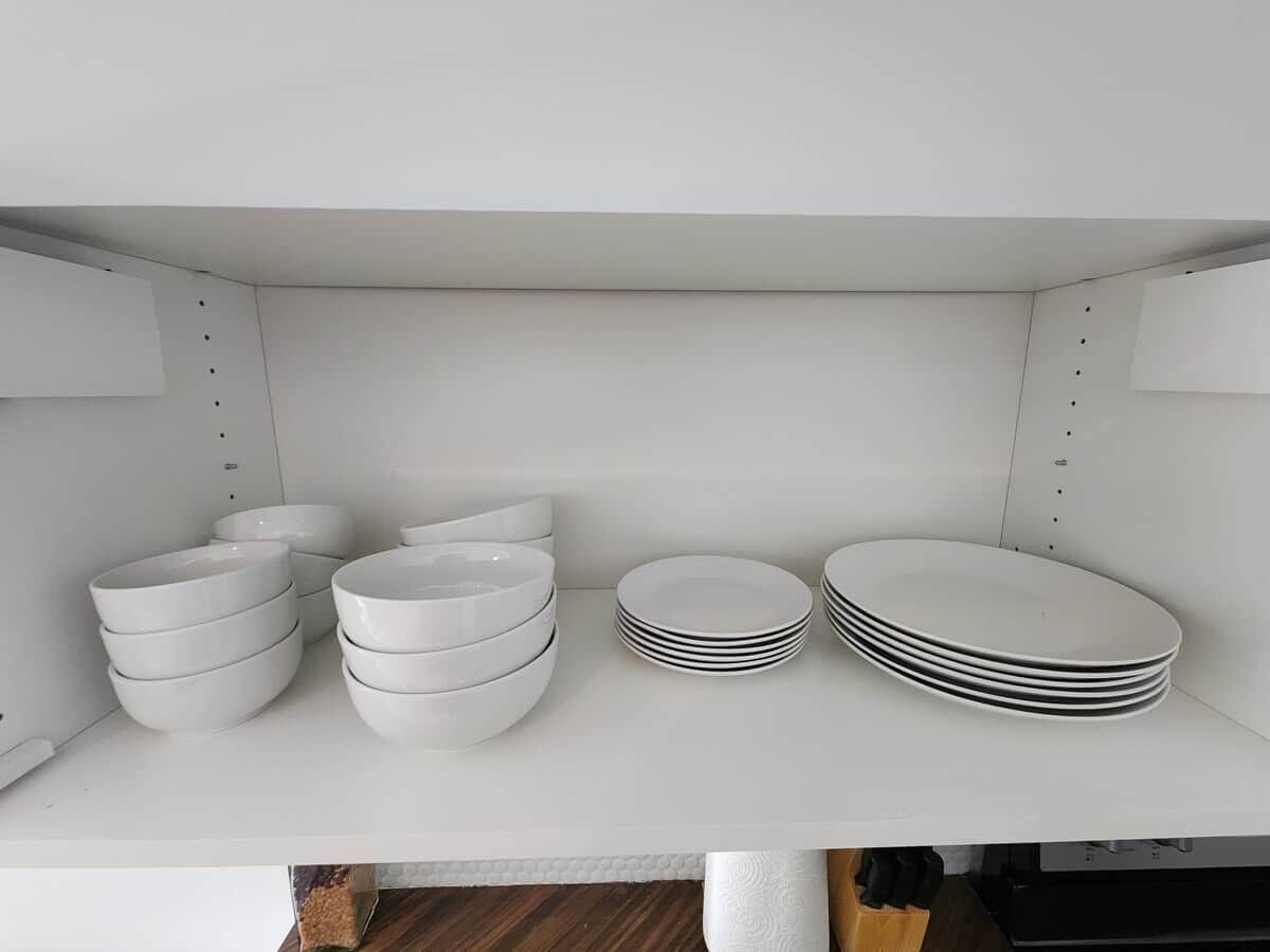 Une étagère blanche sur laquelle sont empilés des bols et des assiettes blancs.