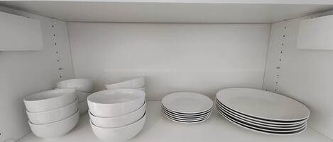 Une étagère blanche sur laquelle sont empilés des bols et des assiettes blancs.