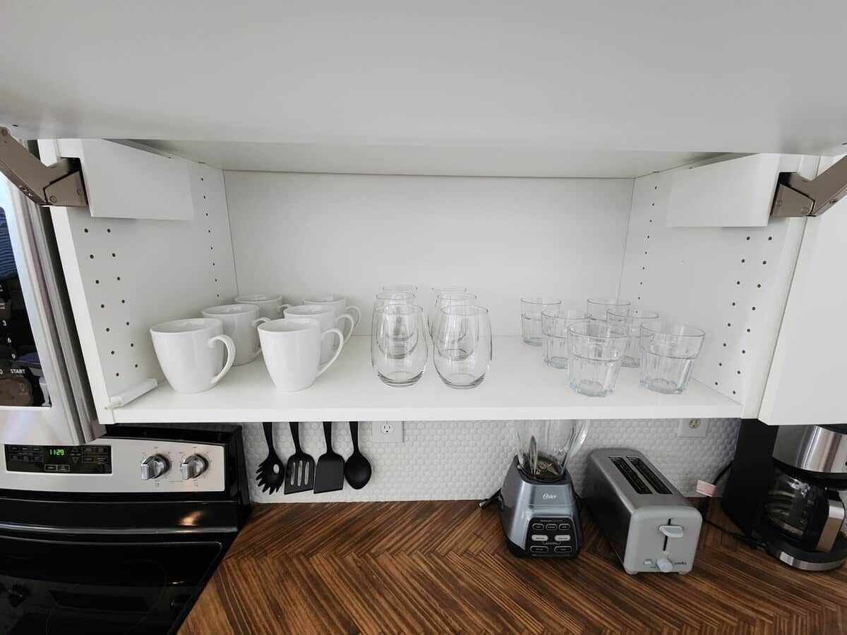 Una cocina con armarios blancos, un microondas, un tostador y diferentes vasos.