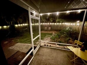 Ett takförsett utomhusområde med ett bord och stolar, en liten trädgård och ljusslingor.