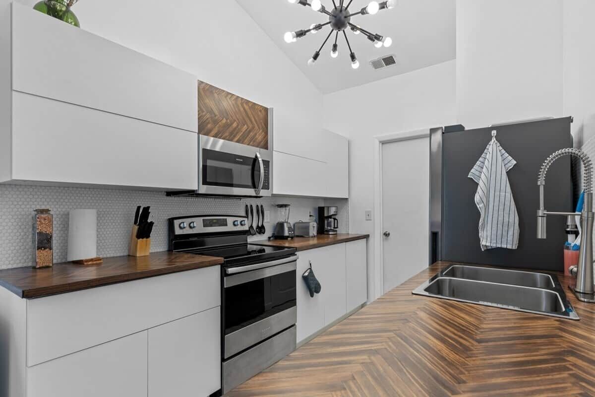 A modern kitchen with white cabinetry, a wooden countertop, a built-in microwave, and a stainless steel sink.