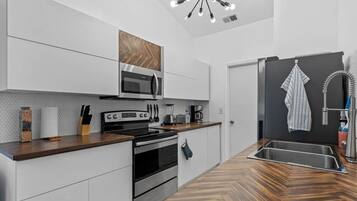 A modern kitchen with white cabinetry, a wooden countertop, a built-in microwave, and a stainless steel sink.