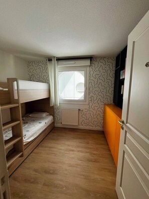 A small, single-room apartment with a bunk bed, a radiator, a window with curtains, and a door with a handle. - Arcachon, luxury apartment, first-row ocean view (ARCACHON)