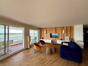 A modern living room with a large TV, wooden panel walls, and a view of the sea. - Arcachon, luxury apartment, first-row ocean view (ARCACHON)