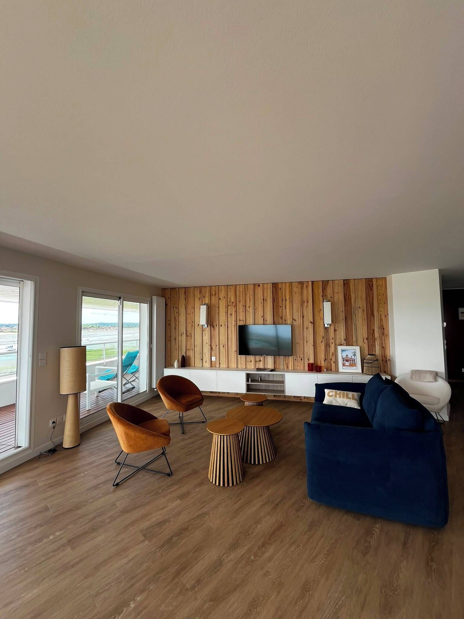 A modern living room with a flat-screen TV, wooden panel wall, and a view of the outdoors.