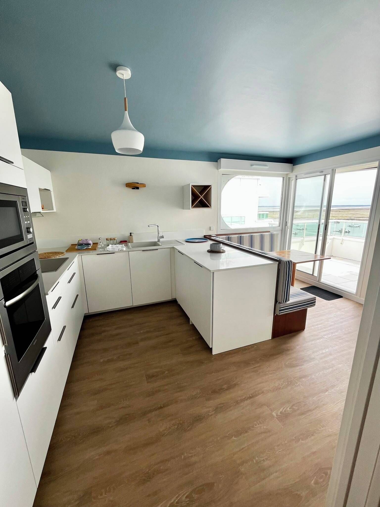 A modern kitchen with white cabinetry, a built-in oven, and a window overlooking a balcony.