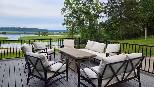 A deck with outdoor furniture, including a sofa and chairs, overlooking a body of water and greenery.