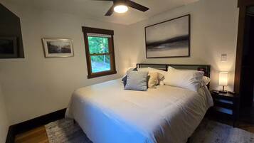 A bedroom with a bed, a window, a ceiling fan, and a nightstand with a lamp.
