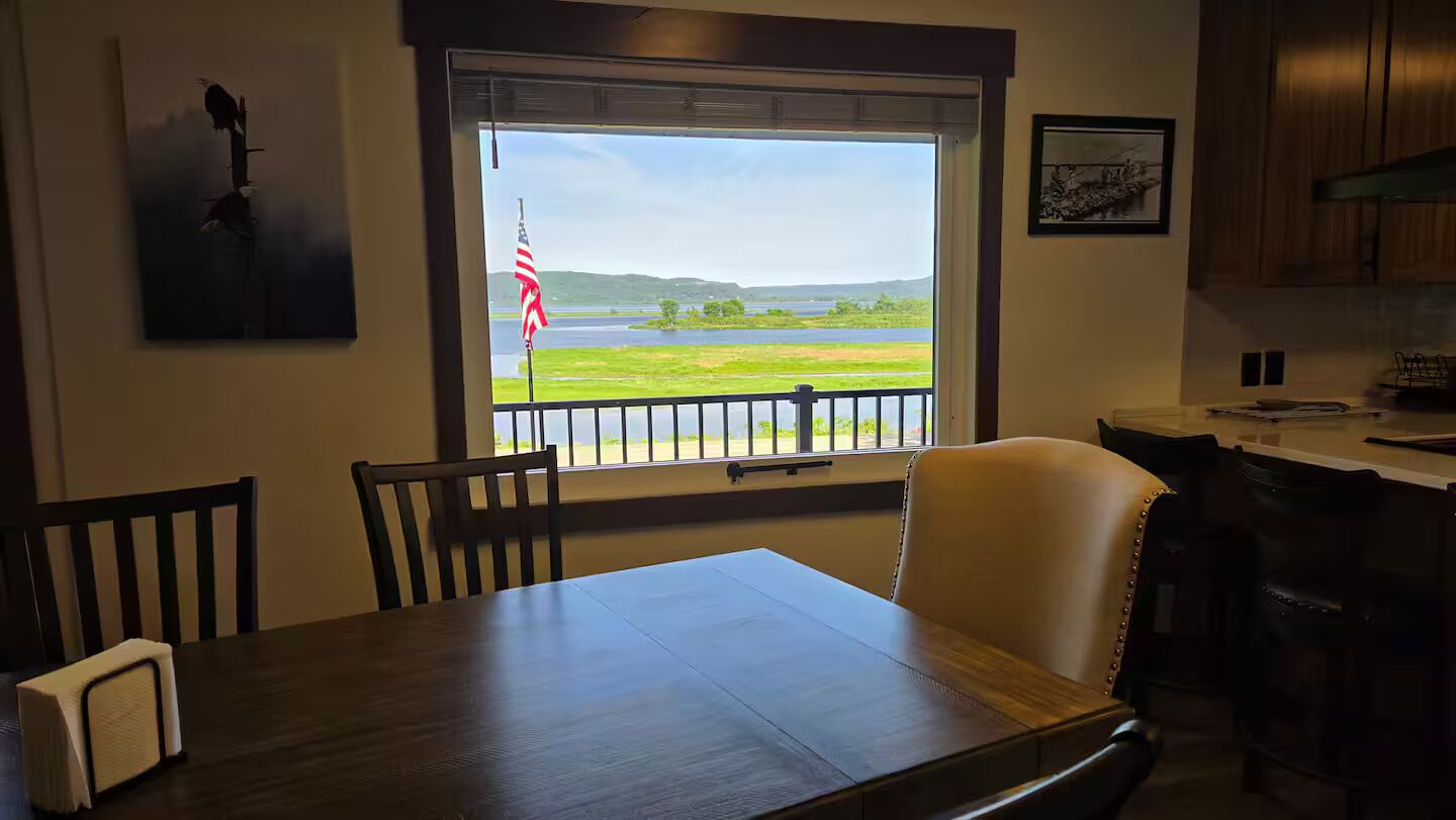 Un comedor con vistas a un lago y colinas, una bandera y un cuadro en la pared.
